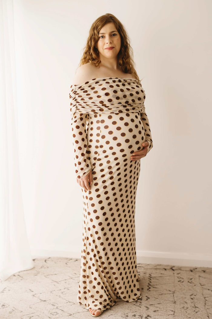 A pregnant lady wearing the Mama Rentals AFRM Thelma Off Shoulder Mesh Maxi Dress in Gold in a studio.