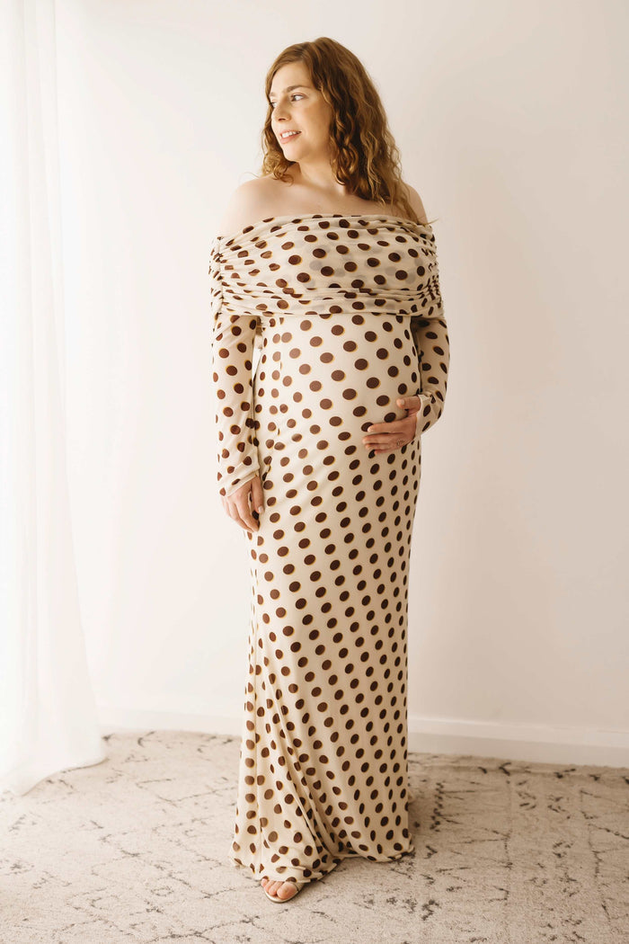 A pregnant lady wearing the Mama Rentals AFRM Thelma Off Shoulder Mesh Maxi Dress in Gold in a studio.