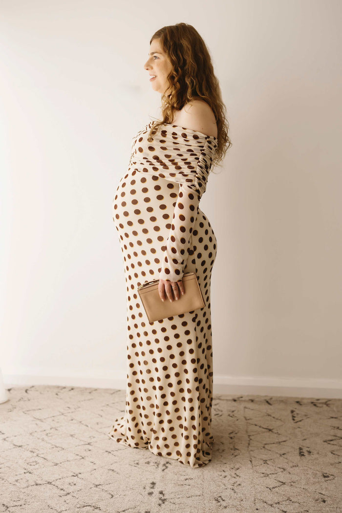 A pregnant lady wearing the Mama Rentals AFRM Thelma Off Shoulder Mesh Maxi Dress in Gold sideways in a studio.
