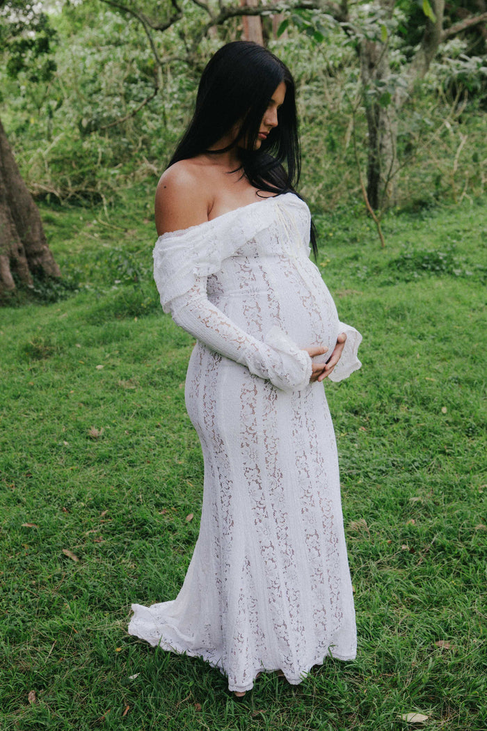 Mama Rentals House of CB Belle Vintage Cream Floral Lace Off Shoulder Maxi Dress worn by a pregnant woman during a maternity photoshoot in a natural, green outdoor setting.