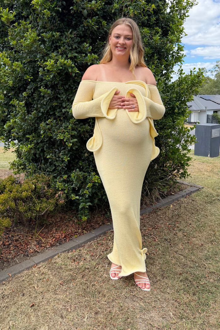 A pregnant lady wearing the Meshki Sandrine Off Shoulder Knit Maxi Dress in Lemon at an event.